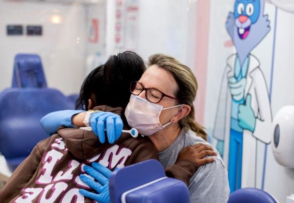 A dental hygienist receives a hug from a girl after a dental screening.